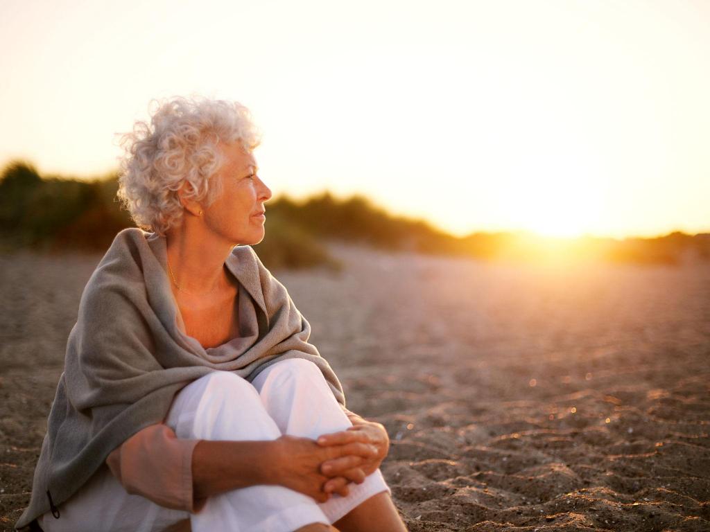 пожилая женщина сидит на песке