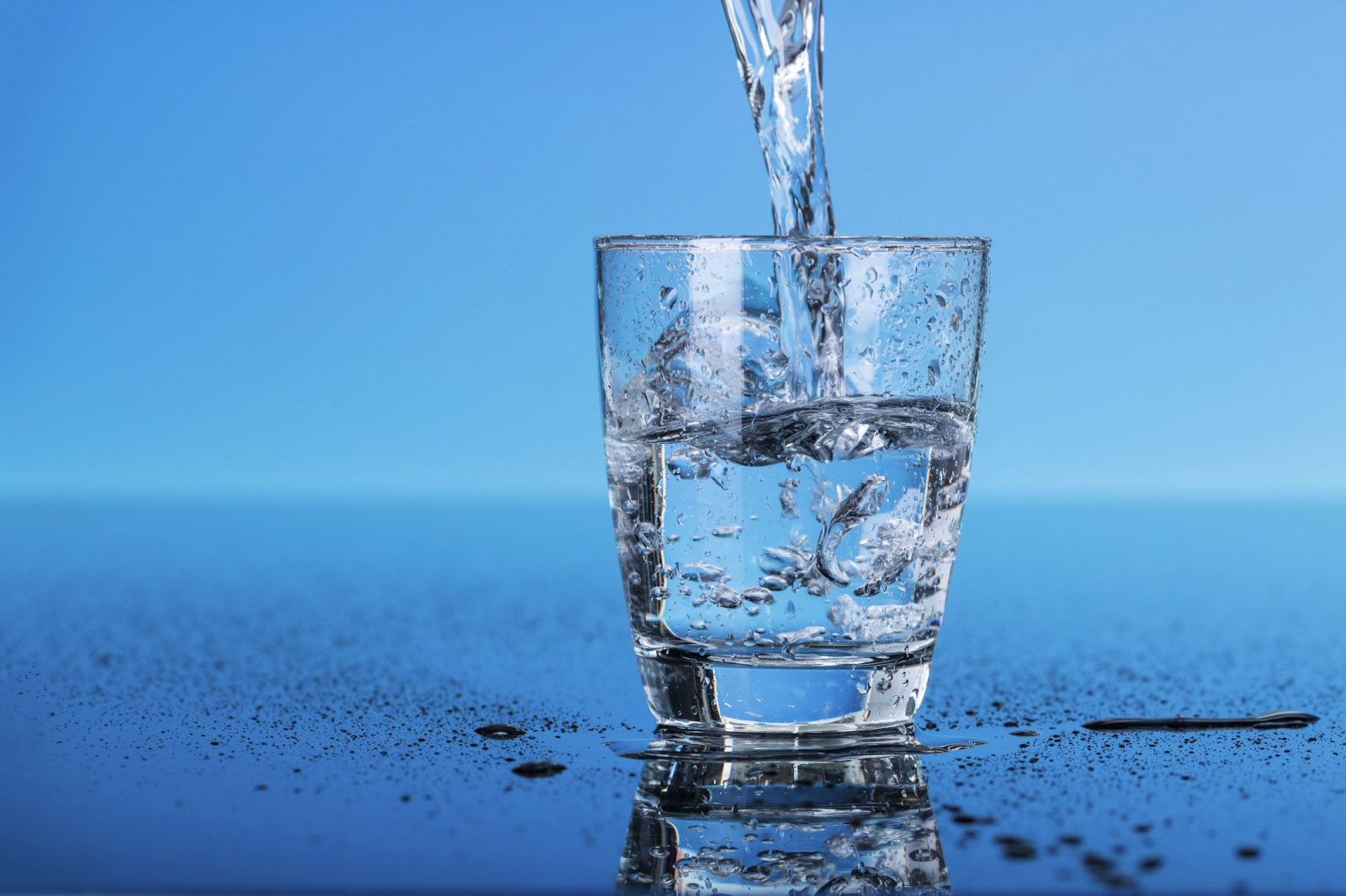 Прозрачный стакан на голубом фоне, в который заливают чистую воду