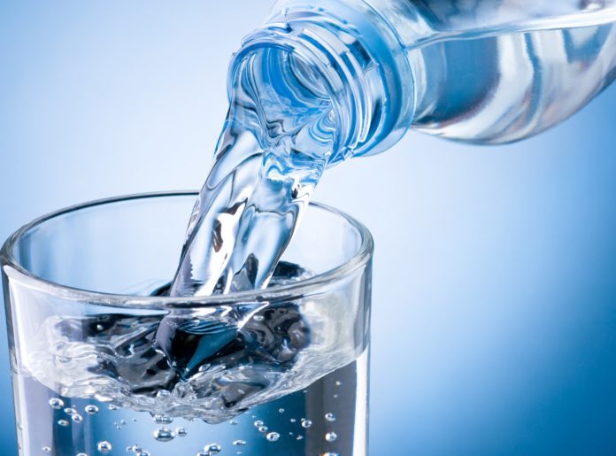 Чистую воду наливают в прозрачный стакан на голубом фоне